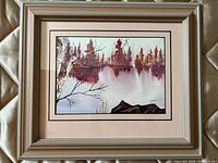 Framed watercolour painting showing autumn trees reflected on water, artist signature visible.