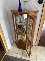 Front view of oak corner display cabinet with door open, two glass shelves and mirrored back visible
