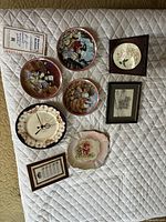 All items laid out on quilted surface showing the variety of plates and framed artworks in the lot.