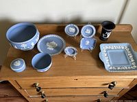 Overview of the Lot Laid Out on Wooden Surface Showing Various Blue and Black Wedgwood Jasperware Items Including Plates, Bowls, Trinket Box, and Vases