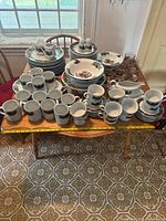 Wide view of whole dinnerware and glassware set on a wooden table, showing mugs, cups, plates, bowls, and glasses with Christmas holly decoration