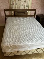 Photo showing the full bed with mattress and box spring, viewed from above and side angle, including headboard design and mattress surface.