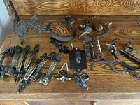 Wide view of miscellaneous antique hardware items arranged on wooden surface showing various handles, hinges, brackets, hooks, and lock plates.