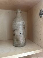Front view of tall gray stoneware crock bottle showing wear and discoloration.