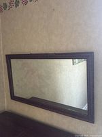 Full view of rectangular mirror with dark wooden frame hanging on a wall showing wear and age.