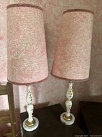 Pair of retro table lamps with pink textured shades and white floral relief ceramic bases on dark wood table.