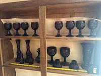 Full display of ruby glass items on wooden shelving showing goblets, decanters, candle holders, and pitcher.