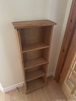 Front view of the wooden short bookshelf showing three shelves and natural wood finish.