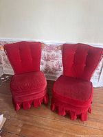 Two antique red parlour chairs side by side against wall showing overall front view.