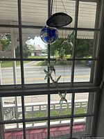 Two hanging sun catchers featuring blue glass globes and multiple hummingbird figures, viewed from a distance and sunlight visible through window.