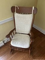 Front view of wooden rocking chair with attached white fabric cushions on seat and backrest.