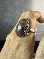 Front-side view of the antique silver ring on finger, showing the large polished brown agate stone with natural patterns and detailed silver scrollwork on ring band.