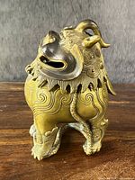 Front three-quarter view of Foo-Lion incense burner showing hinged head, scrollwork mane and patina