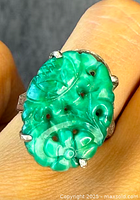 Close-up front view of carved green jade oval ring on finger against grey background