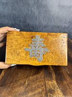 Close-up of burl wood box side with sterling silver Chinese symbol inset on lid, showing wood grain and silver detail.