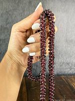Necklace held in hand showing the chunky cluster of small deep red garnet beads.