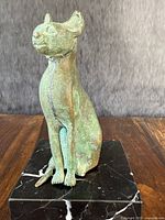 Front-facing view of the antique bronze cat sculpture showing green patina on bronze and marble base with white veins.