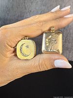Photo showing two antique gold-filled lockets held side by side, front view displaying crescent moon and floral motifs with gemstone accents.