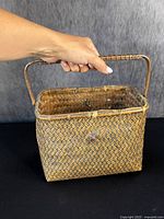 Front view of the antique Japanese Ikebana basket held by hand showing the woven pattern and handle.