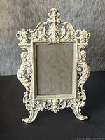 Full front view of antique silvered-metal figural picture frame showing detailed ornamental design and overall shape.