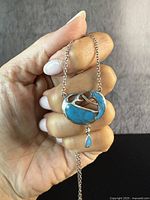 Front view of antique sterling silver pendant with turquoise stones held between fingers showing detail and color.
