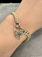Bracelet worn on wrist showing heart padlock front and curb link chain.