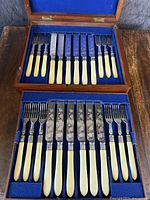 Full view of opened oak box containing knives and forks arranged neatly in blue felt lining.