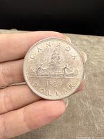 Reverse side of the 1936 Canadian silver dollar depicting the voyageur and Indigenous person paddling a canoe, with date and inscriptions.