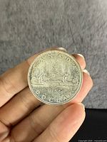 Reverse side of the 1966 Canadian silver dollar coin showing the canoe with two Indigenous people and a voyageur, along with the date and country denomination.