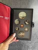 One Canadian silver coin set inside an open black leather folder, showing six coins arranged on black foam backing with red satin lining on the left.