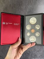 Front side of coin set showing seven Canadian coins including silver dollar, presented in black Royal Canadian Mint case with red interior.