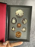 Open black presentation case showing uncirculated Canadian coin set with 7 coins of various denominations and designs including silver dollar and special 25 cent coin.