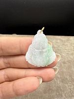 Close-up of carved jade Buddha pendant held between fingers showing front view