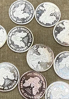 Close-up photo showing the detailed front and back of the silver bullion coins. Various American designs including eagles and figures are visible.