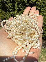 Close-up photo of multiple antique genuine pearl beaded strands with irregularly-shaped pearls, held in hand outdoors.