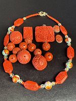 Full set of cinnabar jewelry including necklace and loose beads and pendants on black background.