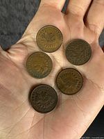 Top side of five pennies showing heads and details in hand.