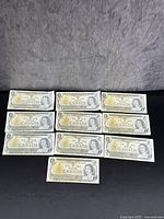 Photo showing all 10 Canadian $1 bank notes arranged in two rows, front side up.