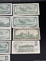 Top angled view showing multiple uncirculated Canadian $1 notes with Parliament buildings engraving on back side