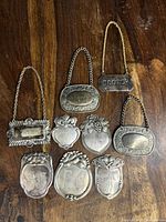 Nine silver decanter tags arranged showing inscriptions and decorative designs