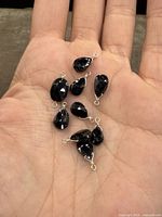 Nine dark blue faceted natural sapphire pendants set in sterling silver displayed on a palm, pear and oval shapes visible.