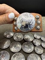 Leather cuff bracelet with silver conchos and Peace dollar laid on fabric with coins