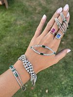 Hand model wearing all pieces showing bracelets, rings, and brooch with green and clear rhinestones