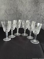 Six crystal wine glasses arranged on black surface against grey backdrop, front view.