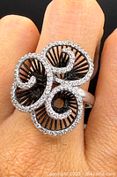 Close-up top view of ring on finger, showing floral swirl design and stone setting