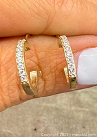 Close-up photo showing the front of both half-hoop earrings with clear stones set along the gold overlay edge.
