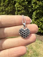 Heart-shaped sterling silver pendant set with natural black sapphires shown being held to display size and detail.