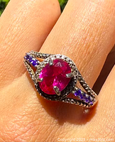Close-up photo of the sterling silver ring on finger showing large central red stone and smaller purple stones on the band.