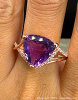 Close-up of the ring showing the trilliant-cut natural amethyst surrounded by clear stones on a rose-gold overlay sterling silver band worn on a finger.