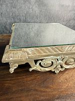 Side angle showing detailed brass scrollwork and leaf carvings on the display stand base with mirrored top.